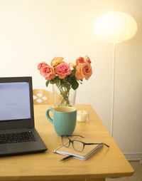 Flower vase by laptop and coffee cup on table at home