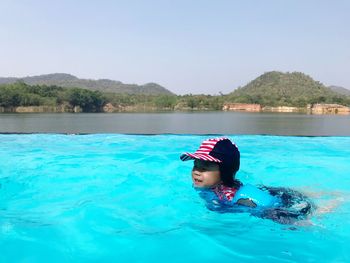 Boy swimming in infinity pool against clear sky