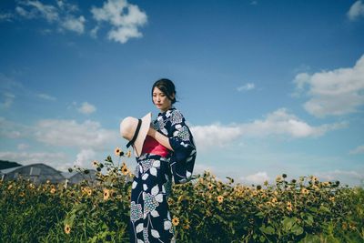 Young woman standing by flowering plants on field against sky