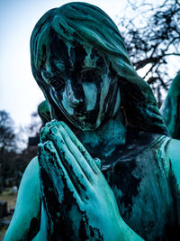 Close-up of angel statue at cemetery against sky