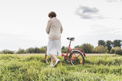 Senior woman pushing bicycle in rural landscape