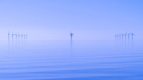 View on wind farm turbines in sun rise haze across still ocean tranquil atmosphere or new energy