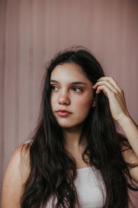 Calm dreamy female teenager with long dark hair standing looking away against plank wall