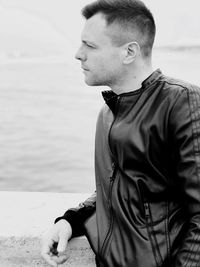 Young man looking away while sitting on beach