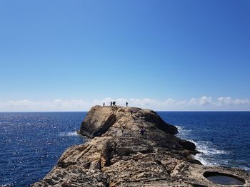 People on rock by sea against blue sky