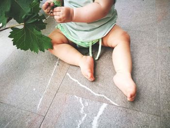 Low section of baby holding leaves while sitting on floor