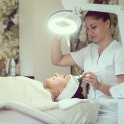 Beautician treating smiling young woman lying on bed
