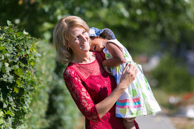 Mother carrying daughter at park on sunny day