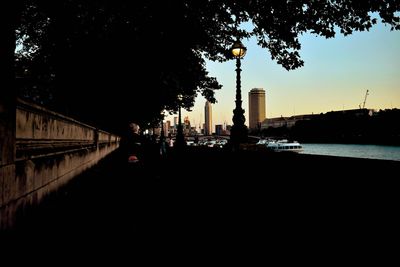 Silhouette buildings by river against sky in city