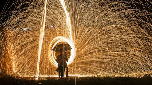 Person carrying umbrella sitting against wire wool on field at night