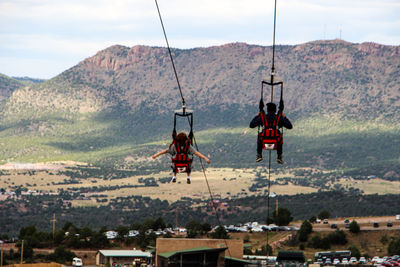 Rear view of people zip lines against mountain