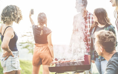 Woman taking selfie with friends against barbecue grill