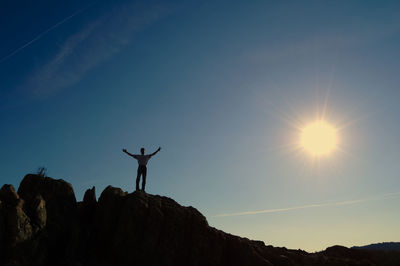 Low angle view of man with arms outstretched standing on mountain during sunny day