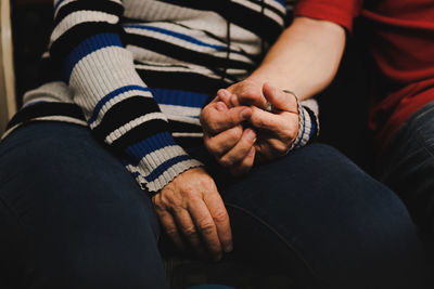 Midsection of man and woman holding hand sitting at home