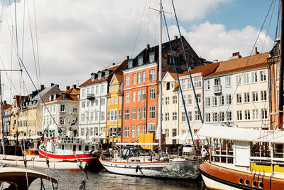 Boats moored in canal by buildings against sky