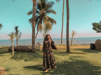 Young woman with palm trees at beach against sky