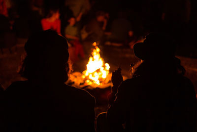 Silhouette couple sitting by bonfire in forest at night