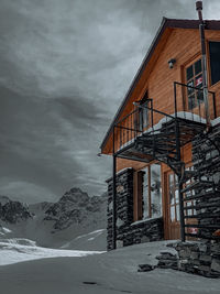Snow covered house by mountain against sky