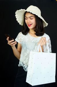 Young woman using mobile phone while standing against black background