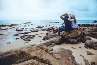 Full length of man sitting on rock at beach against sky