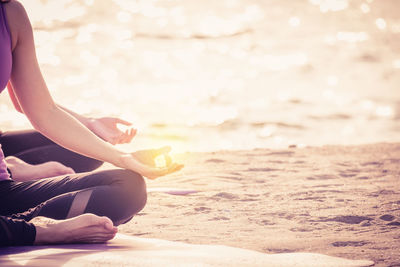 Midsection of woman practicing yoga at beach