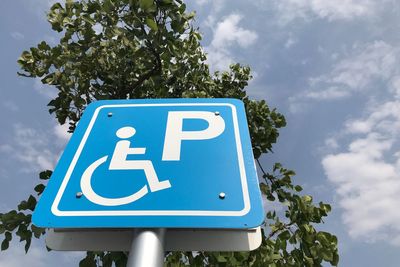 Low angle view of disabled car parking sign against blue sky