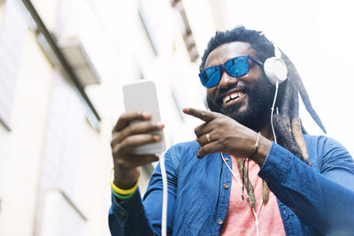 Smiling young man wearing sunglasses listening music on headphones in city