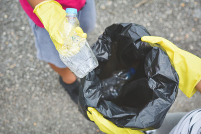 High angle view of people holding crushed bottle and garbage bag while standing on street