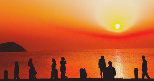 Silhouette people standing on beach against orange sky