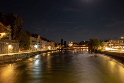 Illuminated buildings by river against sky at night