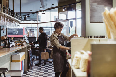 Female store owner working in deli store with customers in background