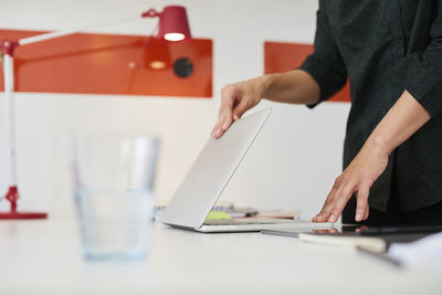 Midsection of mid adult businesswoman opening laptop at table in office