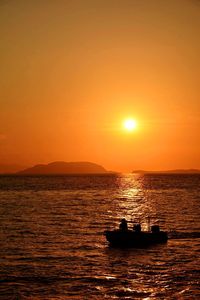 Silhouette person sitting in fishing boat on sea during sunset