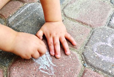 Cropped hands of baby drawing on footpath