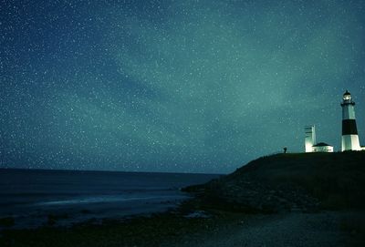 Illuminated montauk point light on shore against star field at night