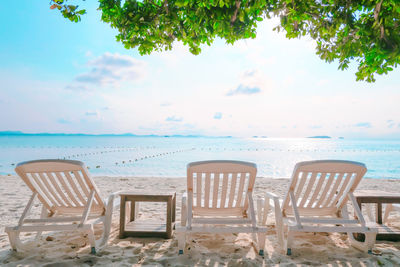 Chairs and table on beach against sky