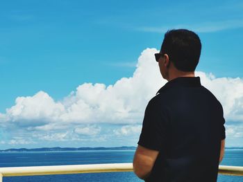 Rear view of man looking at sea against cloudy sky