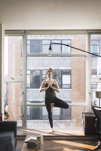 Woman practicing tree pose by window at home