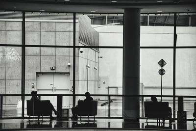 Rear view of people sitting in a large room with glas facade