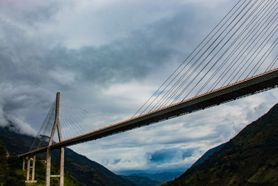 Low angle view of suspension bridge against cloudy sky