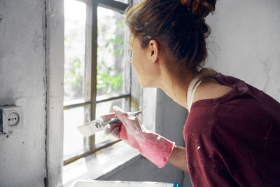 Portrait of woman holding red while standing by window at home
