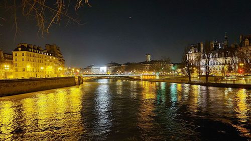 Illuminated buildings by river against sky at night
