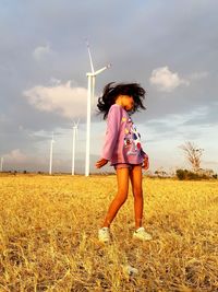 Full length of girl standing on field against wind turbines