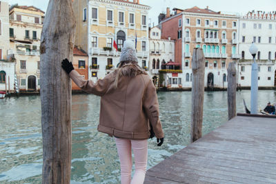 Young woman walking on pier over river against historic buildings