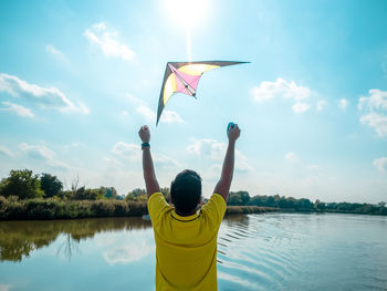 Young man starting to fly bright kite in the sky, photo from back person