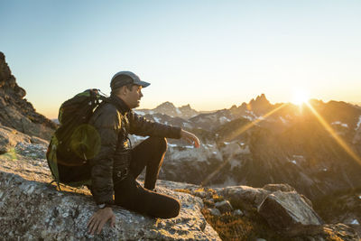 Backpacker sits on mountain summit enjoying view of sunset.