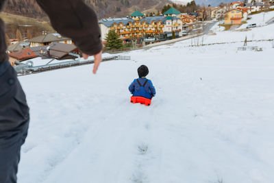 Wide angle view of parent helping child with short dark hair to slide down the snowy hill