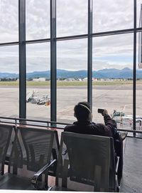 Rear view of man using phone while sitting at airport