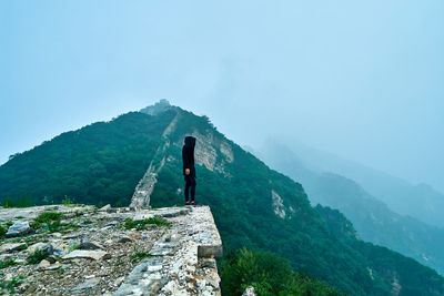 Side view of man standing on mountain against sky