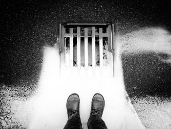 Low section of man standing on road by drainage